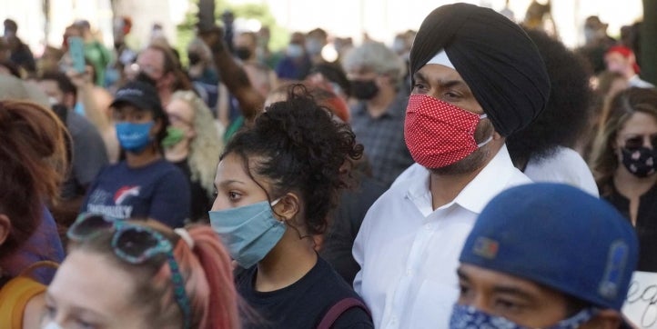 A Sikh man wearing a white shirt, black turban and a red mask stands with other protesters at a march in Kenosha, Wisconsin to support the family of Jacob Blake